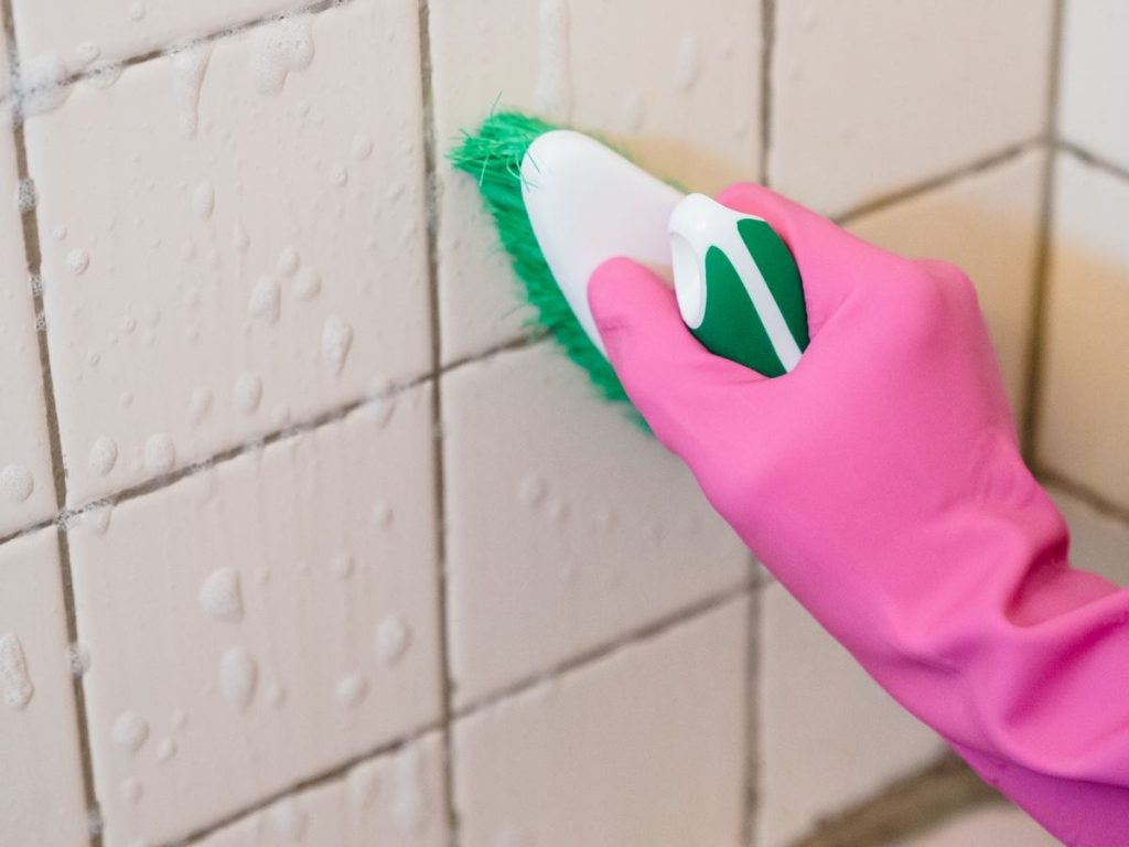 Gloved hand scrubbing wall tiles with a brush