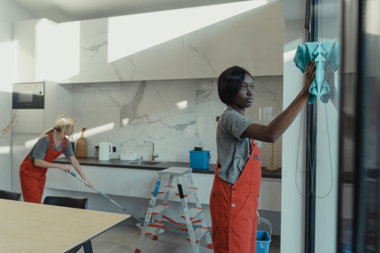 Cleaner wiping kitchen cupboards while a teammate mops